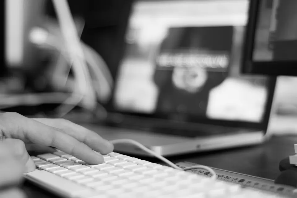 Primer plano de un ordenador portátil negro con teclado y manos trabajando sobre una mesa, fotografía oscura